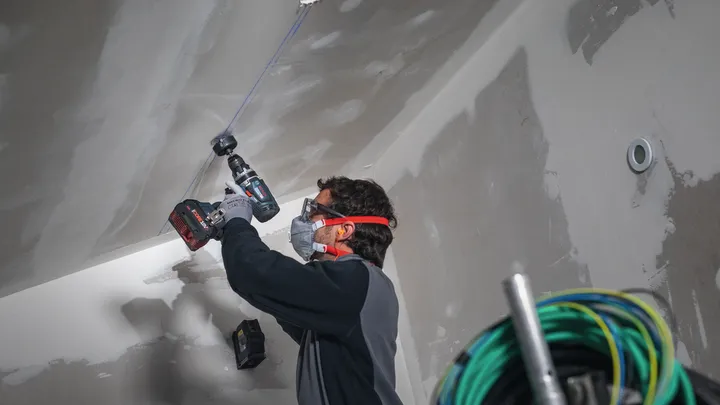 Osoba v bezpečnostním vybavení vrtá do stropu na staveništi.