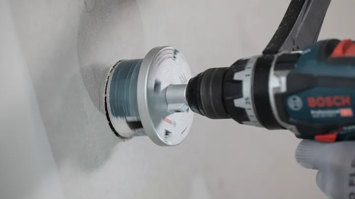 Osoba v bezpečnostním vybavení vyvrtá do zdi velký kruhový otvor.