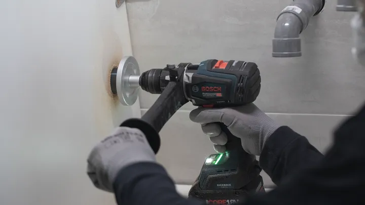 Osoba v bezpečnostním vybavení vyvrtá díru do obložené zdi.