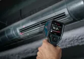 Osoba používající termodetektor k měření teploty vzduchu u větracího otvoru HVAC.