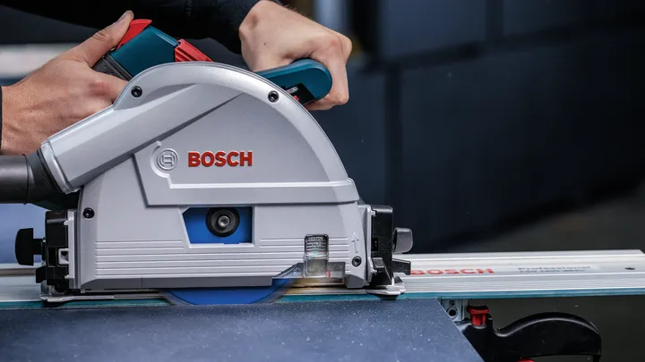 Osoba vede kotoučovou pilu po dráze, aby řezala plech materiálu.