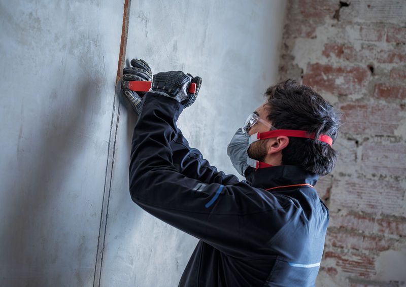 Osoba v bezpečnostním vybavení vytváří kanál v betonu pomocí drážkovací frézy.