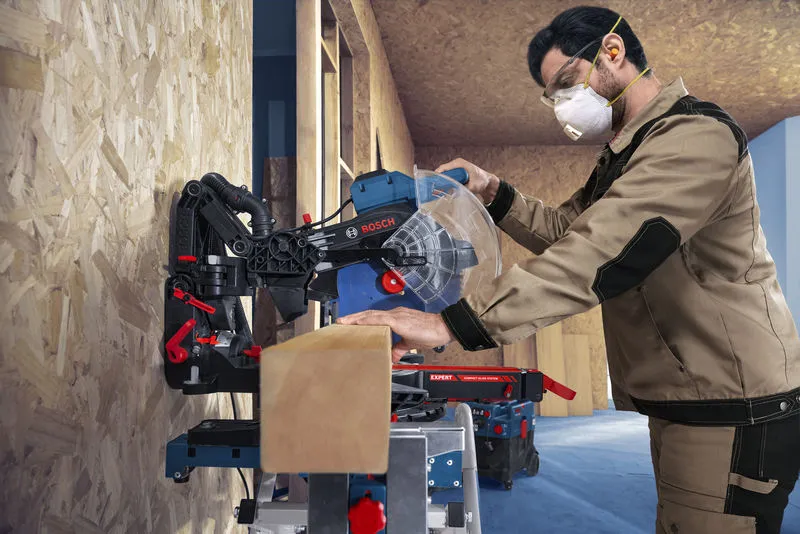 Osoba v bezpečnostním vybavení řeže dřevěný trám pokosovou pilou.