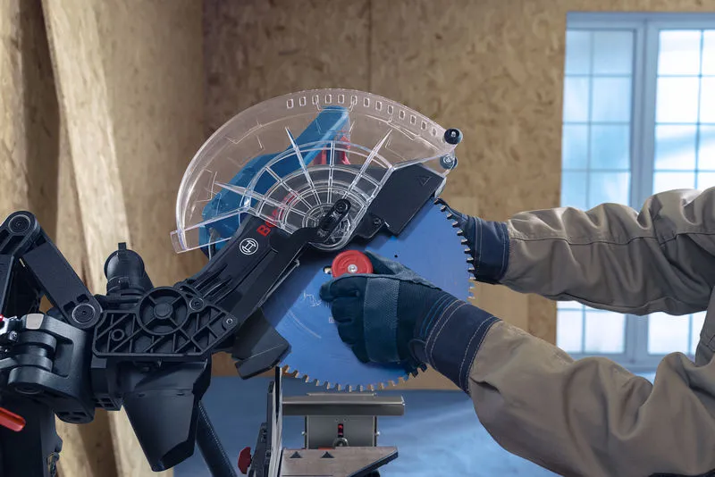 Osoba v bezpečnostním vybavení seřizuje kotouč pokosové pily.