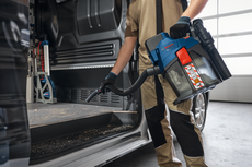 Osoba v bezpečnostním vybavení vysává dřevěné hobliny z interiéru dodávky.