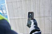Osoba v bezpečnostním vybavení používá laserový měřič poblíž betonové zdi.