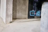 Osoba v bezpečnostním vybavení měří vzdálenost od zdi pomocí laserového měřidla.