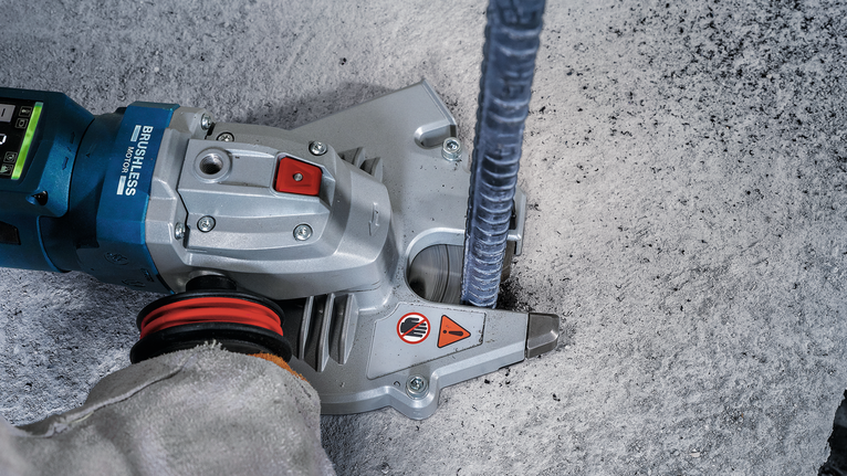 Osoba v bezpečnostním vybavení obsluhuje elektrické nářadí k řezání betonu kolem kovové tyče.