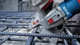 Osoba v bezpečnostním vybavení řeže ocelovou výztuž elektrickým nářadím.