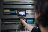 Osoba používá termokameru ke kontrole elektrického ovládacího panelu.