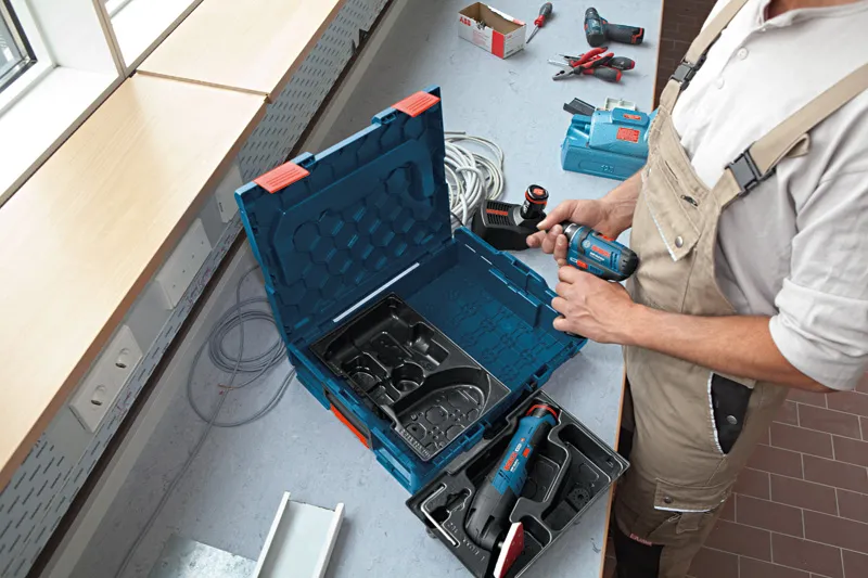 Osoba v bezpečnostním vybavení připravuje na pracovní stanici akumulátorovou vrtačku.