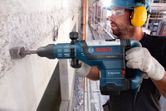Eine Person mit Sicherheitsausrüstung benutzt einen Abbruchhammer, um eine Betonwand aufzubrechen.