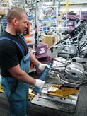 Eine Person mit Sicherheitsausrüstung verwendet ein Elektrowerkzeug, um einen Motorradmotor zusammenzubauen.