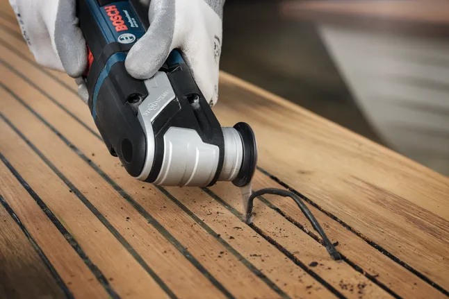 Eine Person mit Sicherheitsausrüstung schneidet mit einem Elektrowerkzeug eine Nut in Holz.