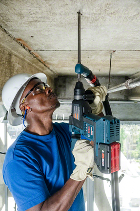 Eine Person in Schutzausrüstung bohrt mit einem Elektrowerkzeug in eine Betondecke.