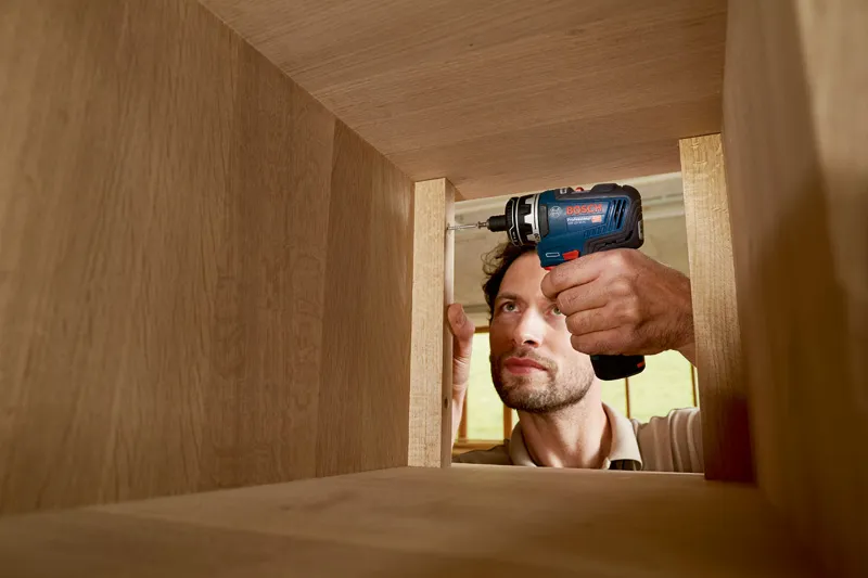 Eine Person verwendet eine Akkubohrmaschine, um einen Holzschrank zusammenzubauen.