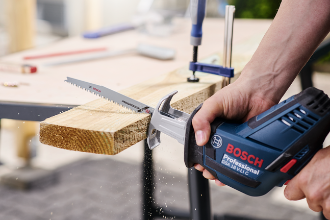 Eine Person benutzt eine Stichsäge, um ein Holzbrett auf einer Werkbank zu zersägen.