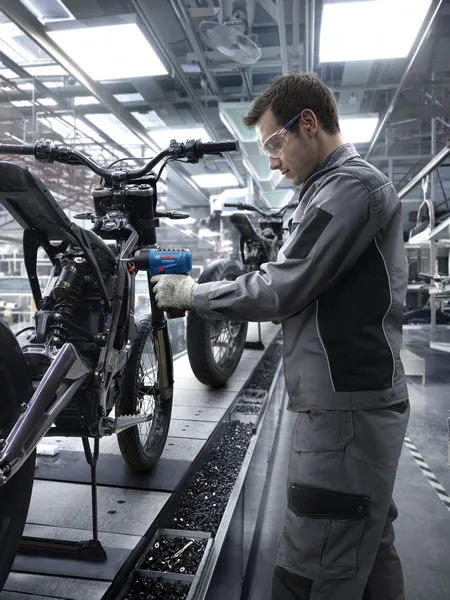 Eine Person mit Sicherheitsausrüstung montiert mit einem Elektrowerkzeug einen Motorradrahmen.