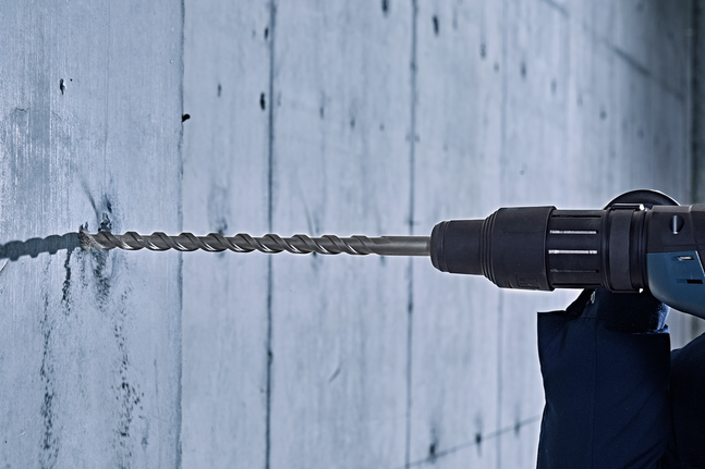 Eine Person in Schutzausrüstung bohrt in eine Betonwand.