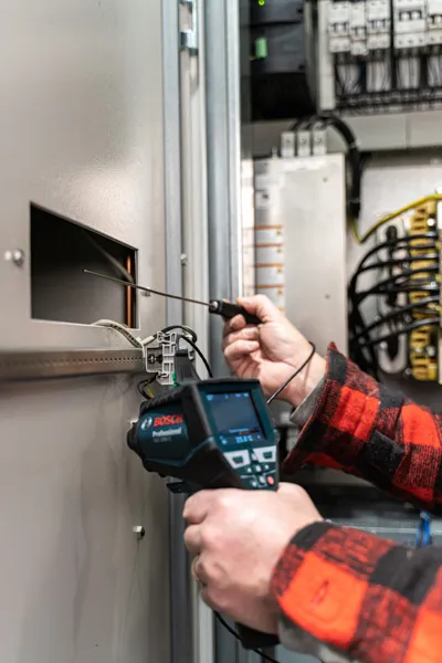 Eine Person verwendet ein Thermodetektor, um elektrische Geräte im Inneren eines Schaltschranks zu überprüfen.
