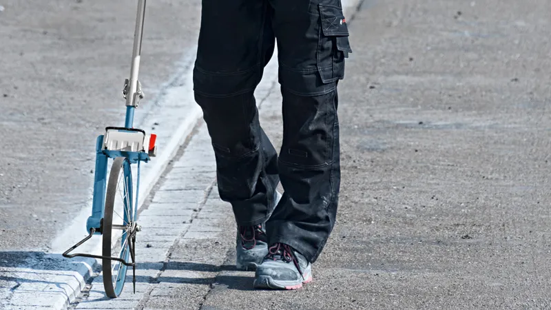 Eine Person mit Sicherheitsausrüstung misst die Straßendistanz mit einem Messrad.