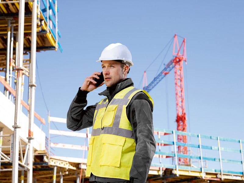 Eine Person mit Sicherheitsausrüstung telefoniert auf einer Baustelle.