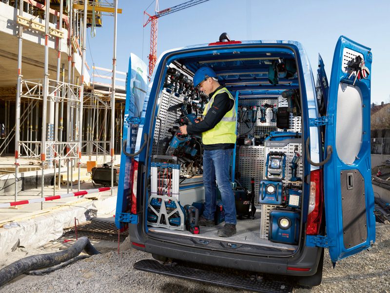 Eine Person in Sicherheitsausrüstung räumt auf einer Baustelle Elektrowerkzeuge in einem Lieferwagen ein.