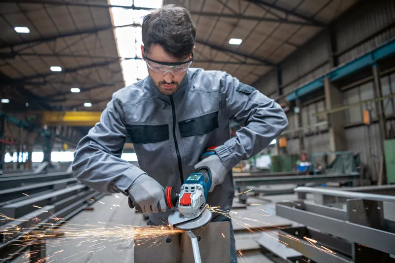 Eine Person, die Schutzausrüstung trägt, schleift Metall mit einem Akku-Winkelschleifer.