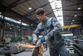 Eine Person, die Schutzausrüstung trägt, schleift Metall mit einem Akku-Winkelschleifer.