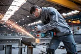 Eine Person, die Schutzausrüstung trägt, schleift Metallträger mit einem Akku-Winkelschleifer.