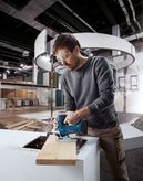 Eine Person, die Schutzausrüstung trägt, benutzt eine Akku-Stichsäge, um Holz in Innenräumen zu schneiden.