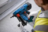 Eine Person mit Sicherheitsausrüstung lädt Nägel in einen blauen Akku-Betonnagler.