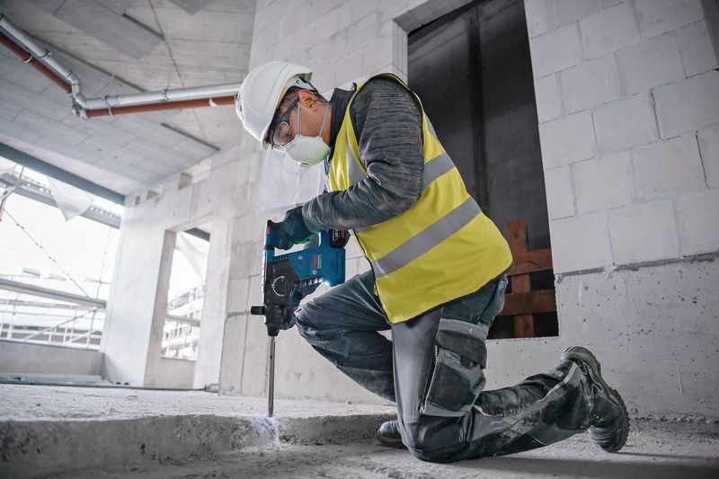 Eine Person mit Sicherheitsausrüstung verwendet einen Bohrhammer, um auf einer Baustelle Beton aufzubrechen.