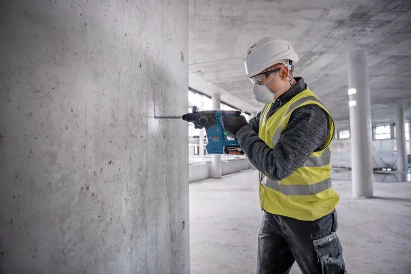 Eine Person mit Sicherheitsausrüstung bohrt auf einer Baustelle in eine Betonwand.