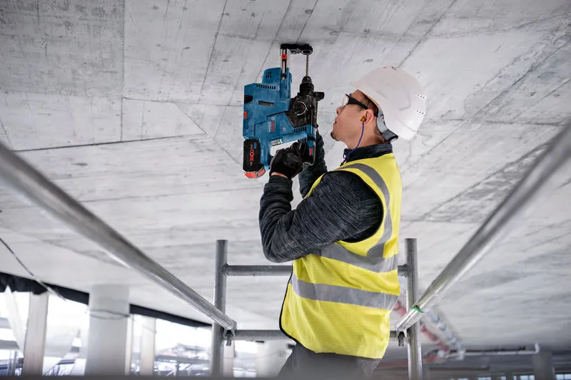 Eine Person mit Schutzausrüstung bohrt mit einem Elektrowerkzeug in eine Betondecke.