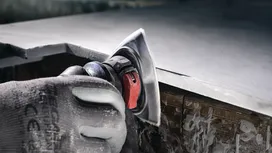 Eine Person mit Schutzausrüstung poliert die Kante einer Arbeitsplatte mit einem Elektrowerkzeug.