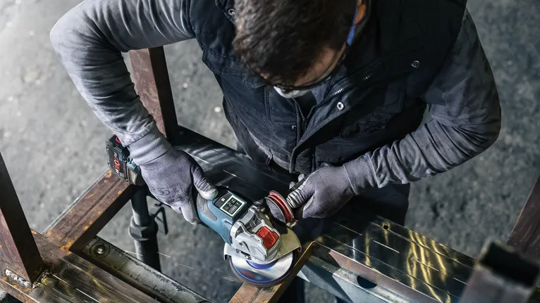Eine Person mit Schutzausrüstung schleift einen Metallträger mit einem Winkelschleifer.