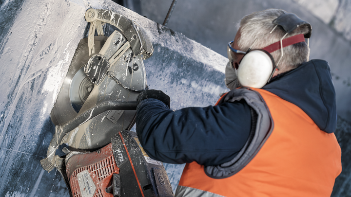 Eine Person mit Sicherheitsausrüstung schneidet mit einer Kreissäge einen großen Betonblock.