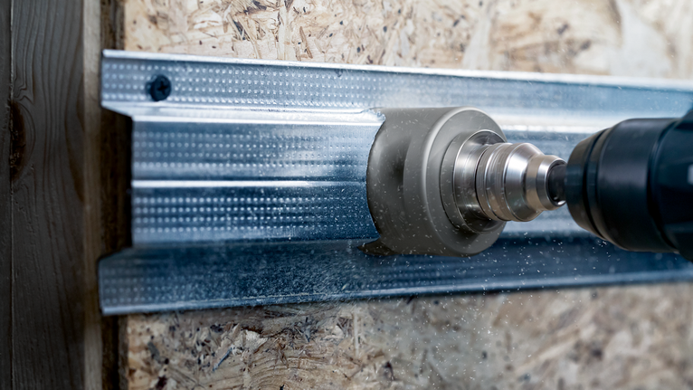 Ein Elektrowerkzeug mit Lochsägenaufsatz schneidet durch einen Metallbolzen.