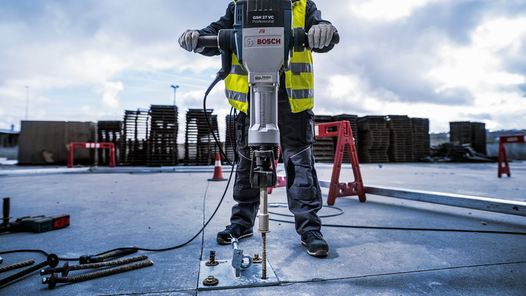 Eine Person mit Sicherheitsausrüstung verwendet einen Abbruchhammer, um Beton im Freien aufzubrechen.