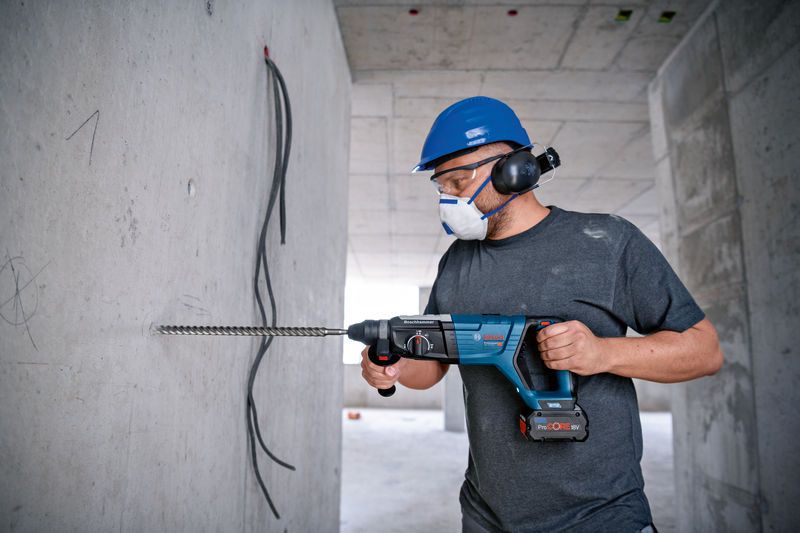 Eine Person mit Schutzausrüstung bohrt mit einem Bohrhammer in eine Betonwand.