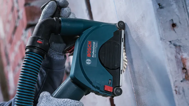 Eine Person mit Sicherheitsausrüstung schleift eine Wand mit einem Elektrowerkzeug.