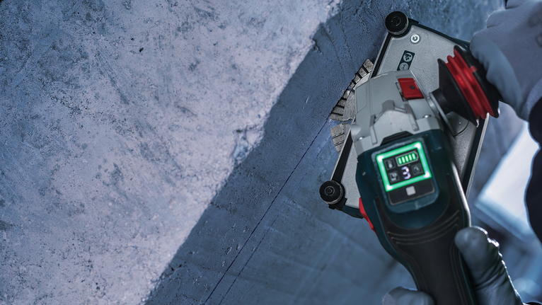 Eine Person mit Sicherheitsausrüstung schneidet mit einem Elektrowerkzeug eine Rille in Beton.