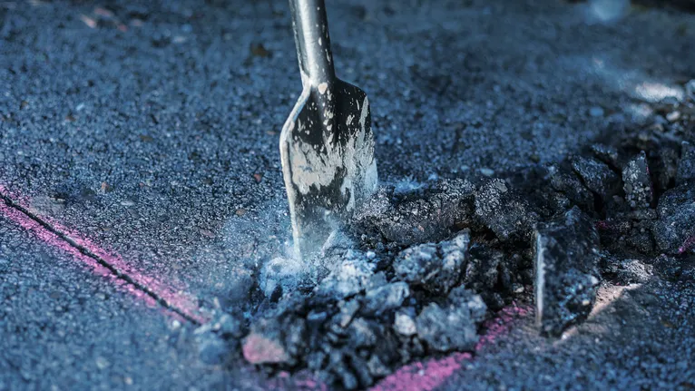 Ein Meißelaufsatz bricht Asphalt entlang einer markierten Linie auf.