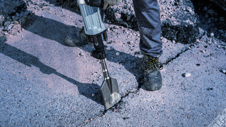 Eine Person mit Sicherheitsausrüstung zertrümmert Beton mit einem Abbruchhammer.