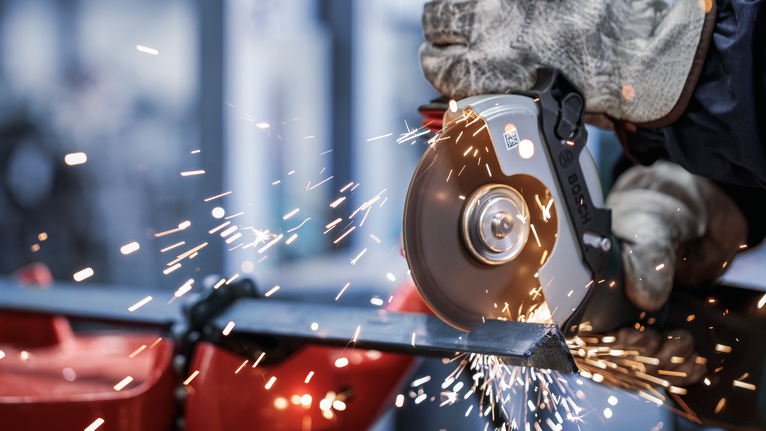 Eine Person mit Sicherheitsausrüstung verwendet einen Winkelschleifer zum Schneiden von Metall, wobei Funken entstehen.