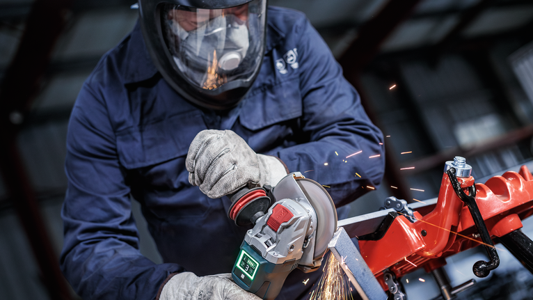Eine Person mit Schutzausrüstung schleift Metall und erzeugt dabei Funken.