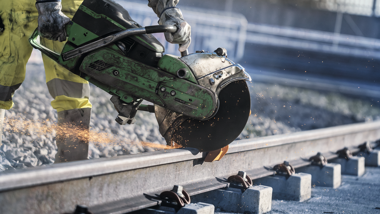 Eine Person, die Schutzausrüstung trägt, benutzt eine Kreissäge, um eine Metallschiene zu durchtrennen.