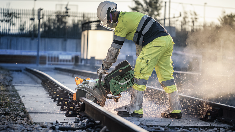Eine Person, die Schutzausrüstung trägt, benutzt einen Motortrennschleifer, um ein Bahngleis zu durchtrennen.