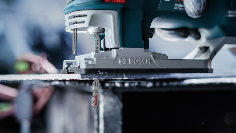 Eine Person mit Sicherheitsausrüstung führt eine Stichsäge und schneidet durch ein Metallblech.